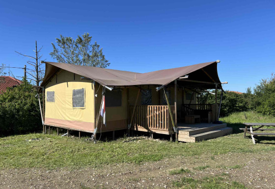 Safari Glamping-Zelt mit Veranda auf einer Wiese, unter klarem Himmel, neben einem Picknicktisch.