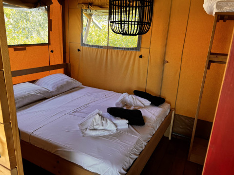 Interior de tienda glamping safari con cama doble y ventanas en Per Amore del Vino, Italia.