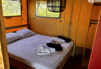Interior de tienda glamping safari con cama doble y ventanas en Per Amore del Vino, Italia.