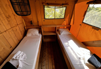 Interior de una tienda glamping safari en Per Amore del Vino, Italia, con dos camas individuales y ventanas grandes.