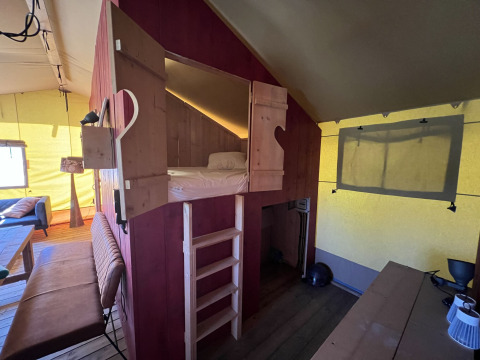 Interior de tienda glamping en Per Amore del Vino, Italia, con cama elevada, escalera y zona de estar.