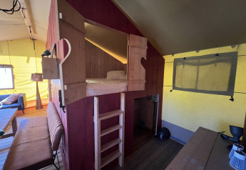 Interior de tienda glamping en Per Amore del Vino, Italia, con cama elevada, escalera y zona de estar.