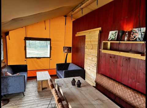 Interior acogedor de una tienda safari glamping en Per Amore del Vino, Italia, con muebles rústicos de madera.