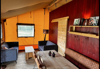 Interior acogedor de una tienda safari glamping en Per Amore del Vino, Italia, con muebles rústicos de madera.