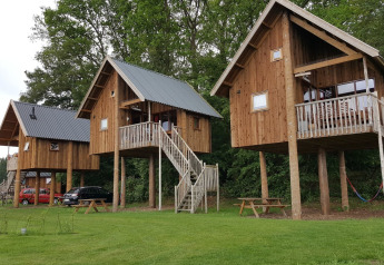 Tree houses on stilts at Camping de Koeksebelt, Netherlands, surrounded by trees and grassy area.