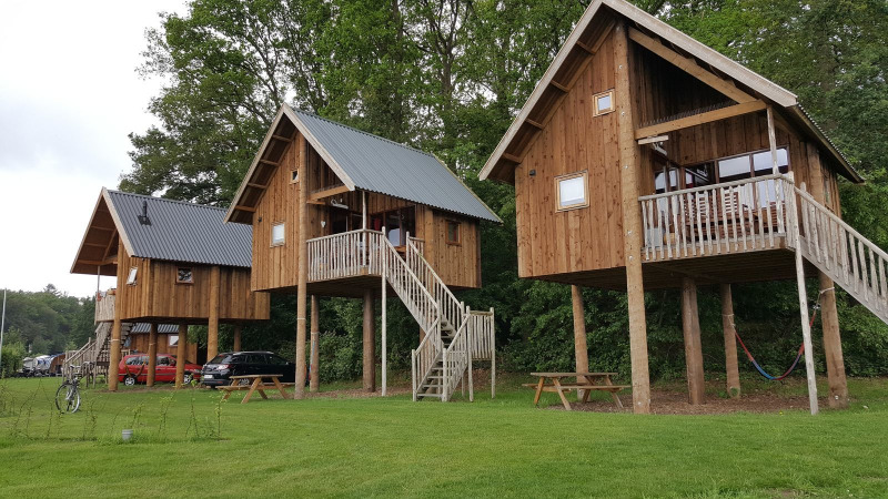 Boomhutten op palen bij Camping de Koeksebelt, Nederland, omgeven door gras en bomen.