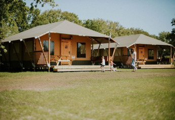 To safari-telte på Camping Si-Es-An i Holland, børn leger udenfor, omgivet af grøn natur og sollys.