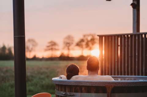 Couple profitant d’un bain à remous extérieur au Wellness lodge d’Ackerlodges Ruinerwold BV aux Pays-Bas au coucher du soleil.