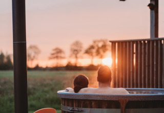 Couple profitant d’un bain à remous extérieur au Wellness lodge d’Ackerlodges Ruinerwold BV aux Pays-Bas au coucher du soleil.