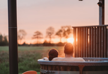 Couple profitant d’un bain à remous extérieur au Wellness lodge d’Ackerlodges Ruinerwold BV aux Pays-Bas au coucher du soleil.