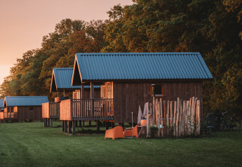 Wellness lodge ved Ackerlodges Ruinerwold BV i Holland med træhytter og frodigt grønt baggrund i solnedgang.