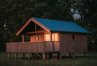 Houten wellness lodge met blauw dak en veranda bij zonsondergang aan Ackerlodges Ruinerwold BV in Nederland.