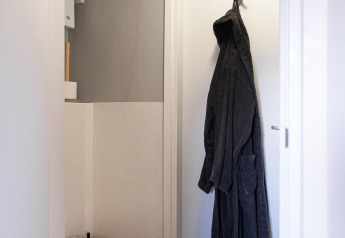 Lille badeværelse med væghængt toilet og mørk badekåbe på en hvid dør i Wellness Lodge, Ackerlodges Ruinerwold BV.