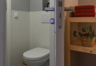 Baño moderno con inodoro suspendido, paredes grises y toallas en la Wellness Lodge Ackerlodges.