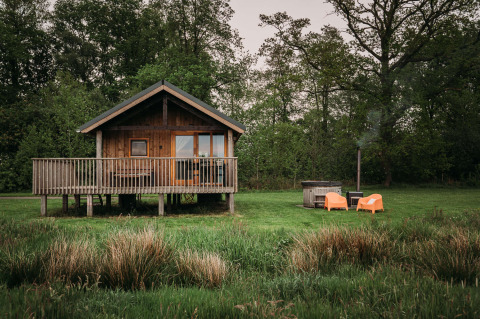 Wellness lodge avec cabane en bois, terrasse, chaises orange et bain nordique extérieur dans la verdure.