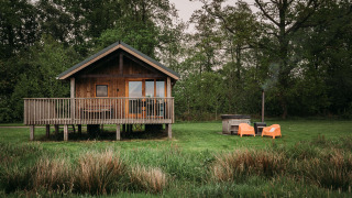 Wellness lodge med træhytte, veranda, orange stole og udendørs badekar omgivet af grøn natur.