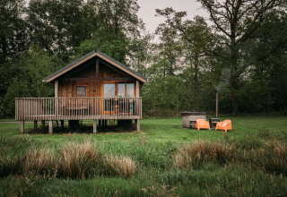 Wellness lodge avec cabane en bois, terrasse, chaises orange et bain nordique extérieur dans la verdure.