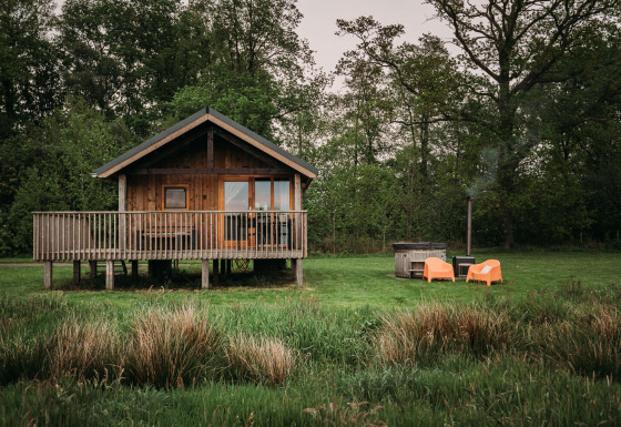 Wellness lodge avec cabane en bois, terrasse, chaises orange et bain nordique extérieur dans la verdure.