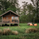 Wellness lodge med træhytte, veranda, orange stole og udendørs badekar omgivet af grøn natur.