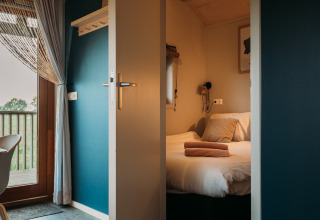 Entrada a una habitación de wellness lodge en Ackerlodges Ruinerwold BV, Países Bajos, con cama y balcón.