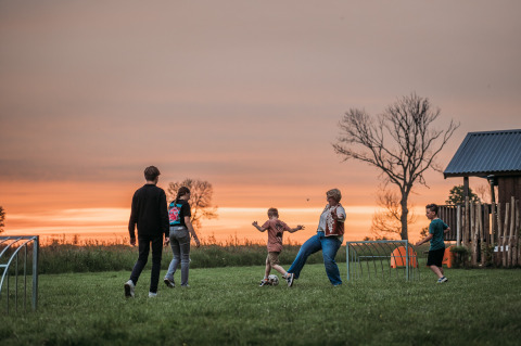Menschen spielen auf einer Wiese Fußball bei Sonnenuntergang an der Wellness Lodge Ackerlodges Ruinerwold BV in den Niederlanden.