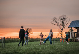 Personas juegan fútbol en un campo de césped al atardecer cerca de Wellness Lodge en Ackerlodges Ruinerwold BV en los Países Bajos.