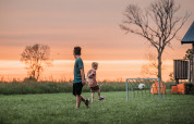 Zwei Kinder spielen Fußball auf einer Wiese bei Sonnenuntergang im Ackerlodges Ruinerwold BV, Drenthe, Niederlande.