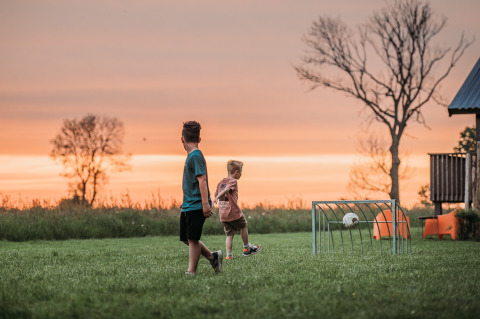Dos niños juegan al fútbol en un campo de césped al atardecer en Ackerlodges Ruinerwold BV, Drenthe, Países Bajos.