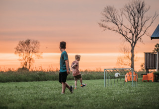 Zwei Kinder spielen Fußball auf einer Wiese bei Sonnenuntergang im Ackerlodges Ruinerwold BV, Drenthe, Niederlande.