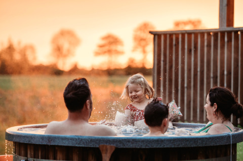 A family enjoys a warm hot tub at sunset at Wellness lodge at Ackerlodges Ruinerwold BV in the Netherlands.