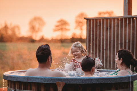 Famille dans un jacuzzi au coucher du soleil au Wellness lodge d’Ackerlodges Ruinerwold BV, aux Pays-Bas.