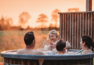 Familie hygger sig i udendørs boblebad ved solnedgang på Wellness lodge ved Ackerlodges Ruinerwold BV, Holland.