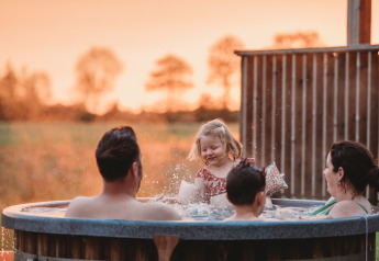 Familie hygger sig i udendørs boblebad ved solnedgang på Wellness lodge ved Ackerlodges Ruinerwold BV, Holland.