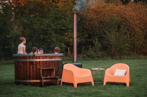 Niños en jacuzzi al aire libre en Wellness Lodge, Ackerlodges Ruinerwold BV, Países Bajos, junto a sillas naranjas.