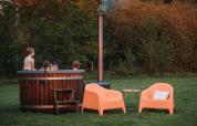 Niños en jacuzzi al aire libre en Wellness Lodge, Ackerlodges Ruinerwold BV, Países Bajos, junto a sillas naranjas.