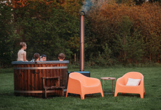 Niños en jacuzzi al aire libre en Wellness Lodge, Ackerlodges Ruinerwold BV, Países Bajos, junto a sillas naranjas.