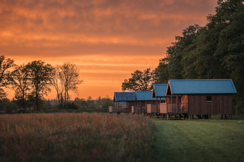 Wellness lodge at Ackerlodges Ruinerwold BV in the Netherlands with wooden cabins and a stunning sunset.