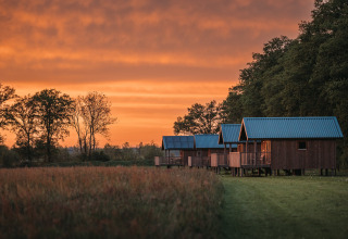 Wellness lodge en Ackerlodges Ruinerwold BV en los Países Bajos con cabañas de madera al atardecer.