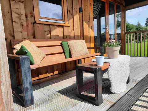 Terrasse extérieure en bois avec banc, coussins et plantes au Wellness lodge d'Ackerlodges Ruinerwold BV, Pays-Bas.