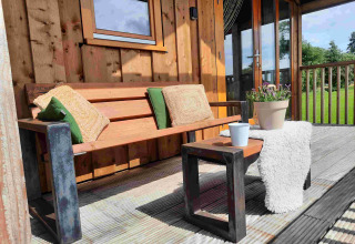 Terraza exterior de madera con banco, cojines y plantas en Wellness lodge de Ackerlodges Ruinerwold BV, Países Bajos.