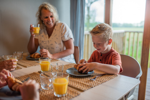 En familie nyder morgenmad med juice og croissanter i Wellness lodge på Ackerlodges Ruinerwold BV i Holland.
