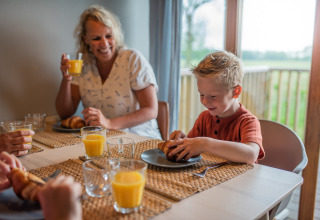 Una familia disfruta del desayuno con jugo de naranja y cruasanes en Wellness lodge de Ackerlodges Ruinerwold BV, Países Bajos.