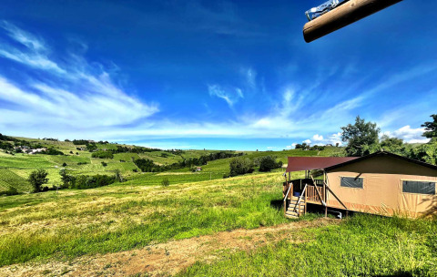 Tienda glamping en Per Amore del Vino, Italia, con vistas a campos verdes y cielo azul brillante.