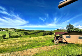 Tienda glamping en Per Amore del Vino, Italia, con vistas a campos verdes y cielo azul brillante.