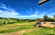 Tienda glamping en Per Amore del Vino, Italia, con vistas a campos verdes y cielo azul brillante.