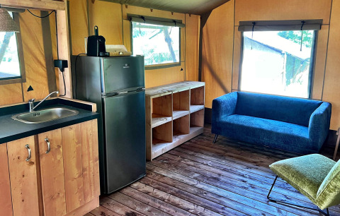Interior de una tienda glamping en Per Amore del Vino, Italia, con cocina pequeña y confortable sofá azul.