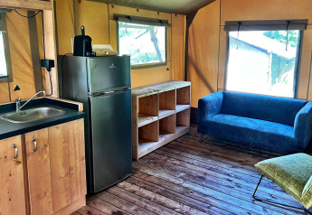 Interior de una tienda glamping en Per Amore del Vino, Italia, con cocina pequeña y confortable sofá azul.