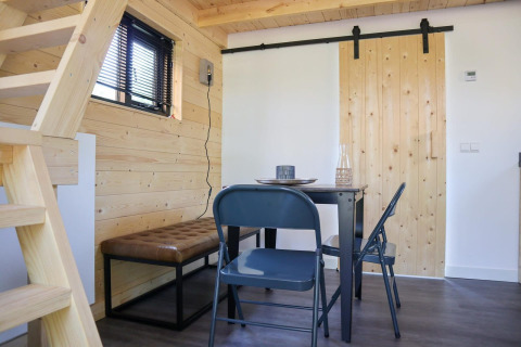 Vista interior de la Tiny House en De Hooge Veluwe con mesa de comedor, sillas plegables y paredes de madera.