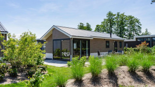 Lodge moderno Velthorst en EuroParcs Veluwemeer, Países Bajos, rodeado de vegetación exuberante y cielo azul.