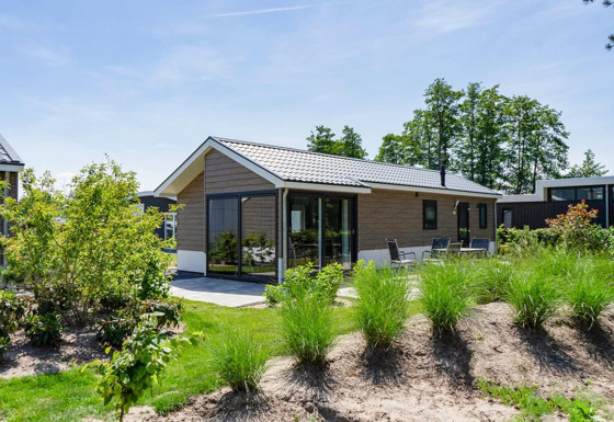 Lodge moderno Velthorst en EuroParcs Veluwemeer, Países Bajos, rodeado de vegetación exuberante y cielo azul.